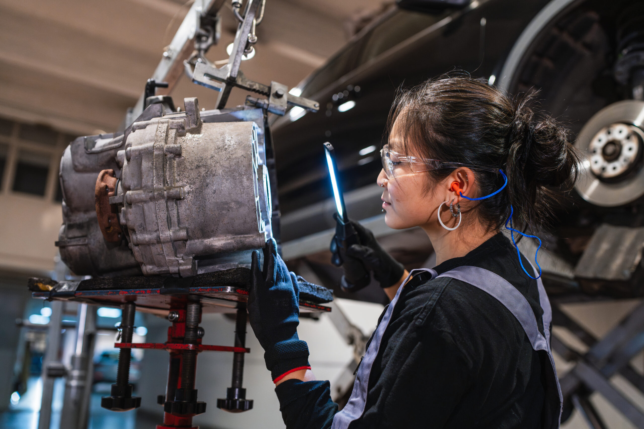 Female Mechanic Inspecting Car Part With Uv Light In Repair Shop